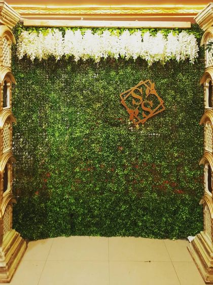 A mantap with ornate pillars and a green foliage backdrop, personalized with a couple's monogram for their baby shower.