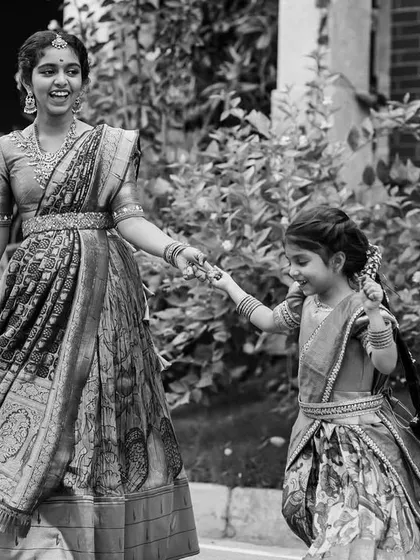 A lovely black and white candid of two sisters in traditional dress, holding hands and walking together. This image captures the simple beauty of their bond and movement.