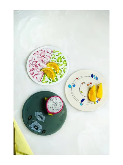 A minimalist flatlay of three different artisanal plates, styled with fresh fruit to highlight their unique designs.