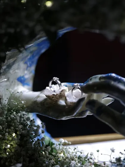 A close-up of a custom wedding ring holder I created, featuring two rings resting on crystals inside a sculpture of two hands, surrounded by preserved flowers and fairy lights.