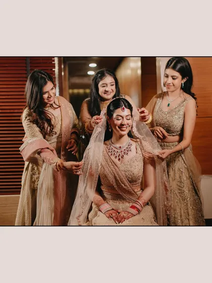 The bride Shreya shares a happy moment with her bridesmaids as they help her with her veil. The genuine smiles and supportive gestures capture the essence of friendship on a wedding day.
