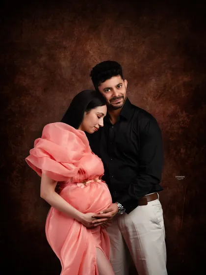 An intimate and tender moment between partners. The close embrace and soft lighting against the dark backdrop create a deeply emotional and romantic maternity portrait.