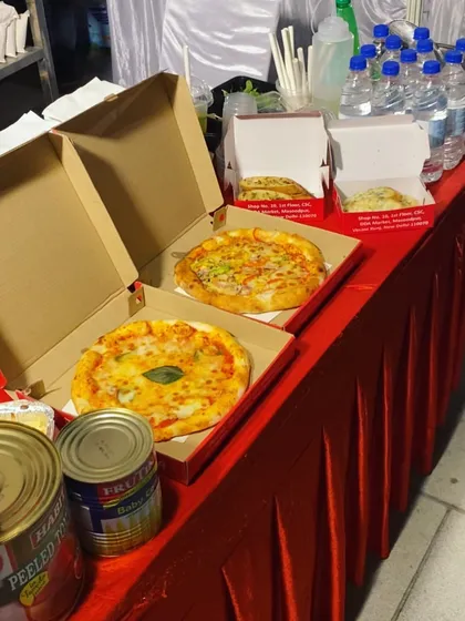 Freshly baked pizzas, one classic Margherita and one loaded with vegetables, ready to be served in boxes at an event. I can handle high-volume orders to ensure all your guests are fed promptly.