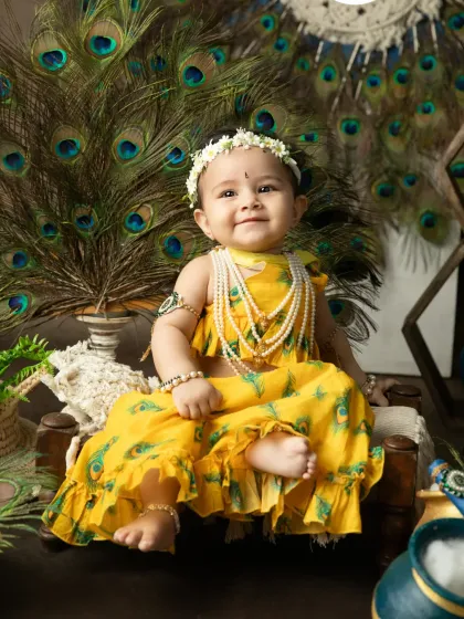 A happy smile from a little girl enjoying the Janmashtami setup, surrounded by peacock feathers.
