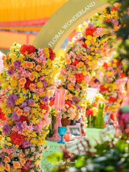 A close-up of a floral archway from a "Floral Wonderland" themed event. The arch is densely packed with a rainbow of flowers, creating a stunning and immersive experience.