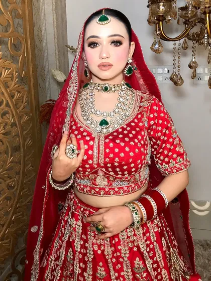 A regal bridal portrait. The bride is wearing a classic red lehenga with a stunning diamond polki and emerald necklace set.