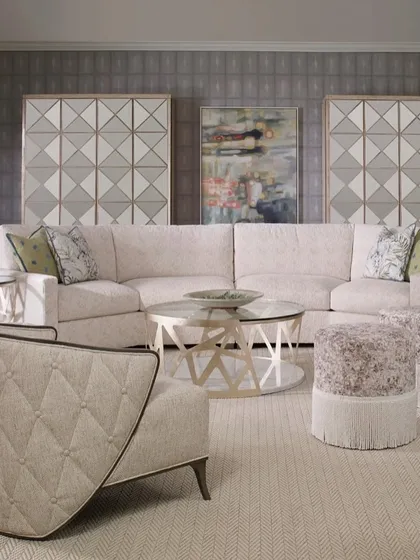 A full living room setting, showcasing our graceful winged lounge chair, a large sectional sofa, and fringed ottomans. The buttoned and tufted detailing on the chair's exterior adds a layer of classic craftsmanship.