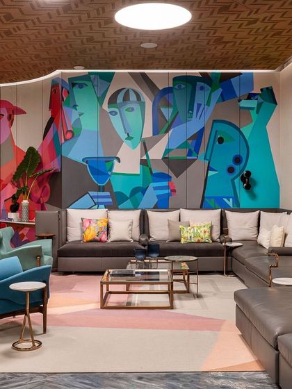 A cubist-style mural in a basement lounge, featuring abstract faces and forms in a cool blue and green palette.