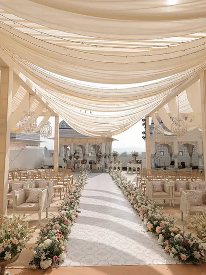 A wedding aisle should feel like a dream. For this serene morning ceremony, we used soft pastel florals and flowing fabrics to create an elegant pathway that perfectly contrasted with the bride's vibrant red attire, leading to a beautifully intimate mandap.