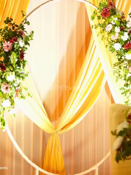 A stunning stage backdrop featuring a circular frame adorned with florals and draped with yellow fabric, perfect for a couple's seating area at a Haldi or reception.