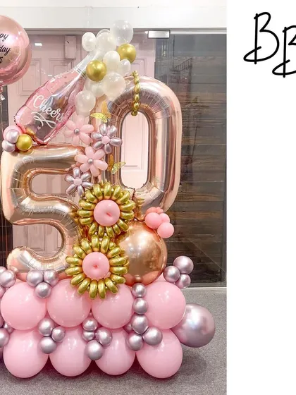 Cheers to 50 years with this pink champagne-themed arrangement. The rose gold '50' is paired with a popping champagne bottle balloon and intricate gold and pink balloon flowers, creating a celebratory and elegant display.