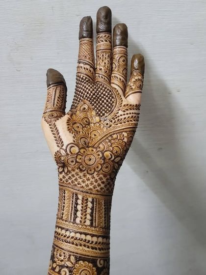 A full view of a detailed bridal henna design, extending from the fingertips to the mid-forearm. This piece combines floral patterns, checks, and bold bands for a traditional yet clean look.