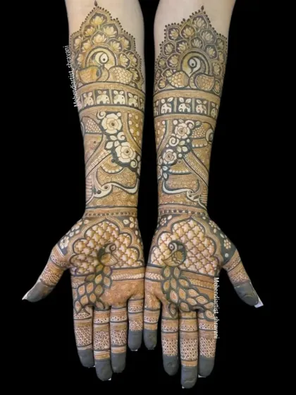 An intricate peacock design covering the hands and forearms. The palms feature a detailed peacock with its feathers spread out in a beautiful pattern.