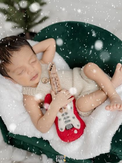 Even the tiniest rockstars need their rest. A newborn holds a mini guitar while sleeping in a snowy, festive setting.