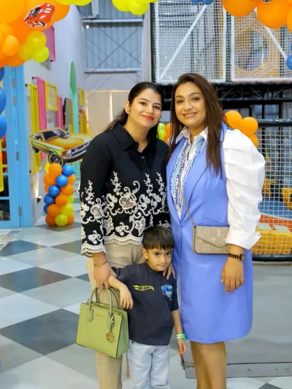 Two mothers and a child pose for a photo at a vibrant, car-themed birthday party.