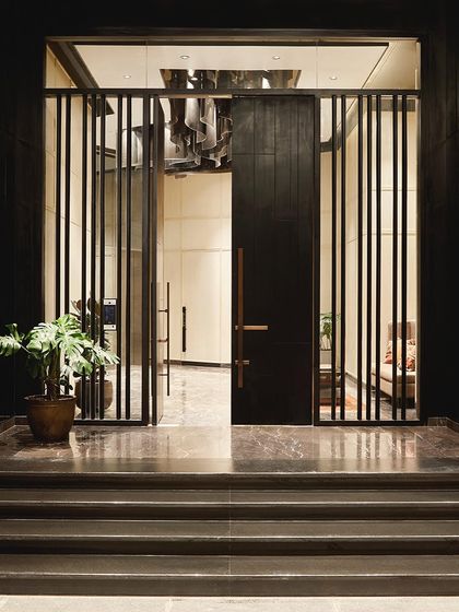 Tall wooden doors mark the entrance to the interior lobby, where a custom glass chandelier guides the flow of movement towards the elevators.