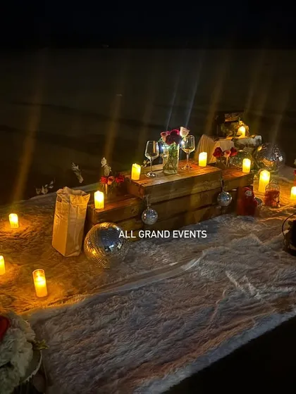 The full picnic setup illuminated by candlelight against the dark beach, creating a magical and intimate oasis for the couple. Every element is placed to be both beautiful and functional.