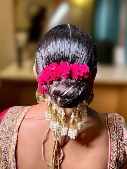 The sleek finish of this bun contrasts beautifully with the soft texture of the pink flowers and the dangling pearl tassels, creating a rich, traditional look.