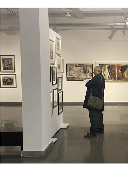 A visitor at the Vidya Bhushan retrospective, studying a dense salon-style hang of smaller works.