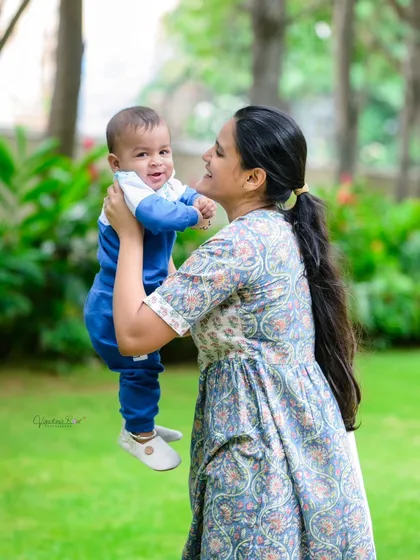 A mother lifts her smiling baby boy during an outdoor photoshoot. The natural greenery and soft light create a perfect backdrop for these happy moments.
