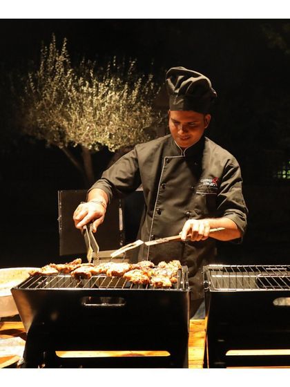 A chef grills skewers over a charcoal barbecue at night. This image, a duplicate of ID 29, reinforces the theme of authentic, open flame cooking that imparts incredible flavour.
