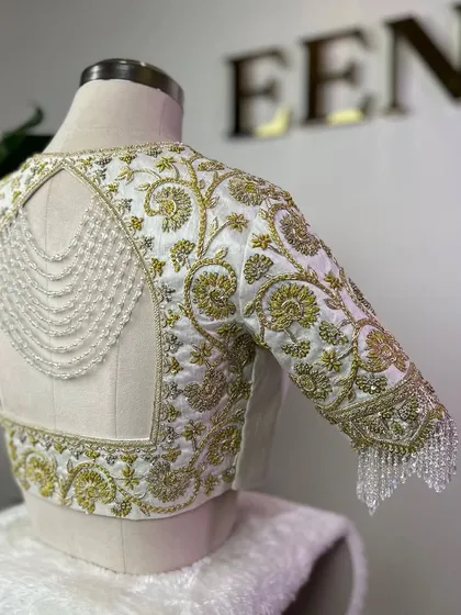 This blouse is a perfect example of my passion for detail. For my client Jhansi, I crafted this piece with intricate gold zardozi embroidery on a white raw silk base, adding a modern touch with a pearl-draped open back and sparkling crystal tassels on the sleeves.