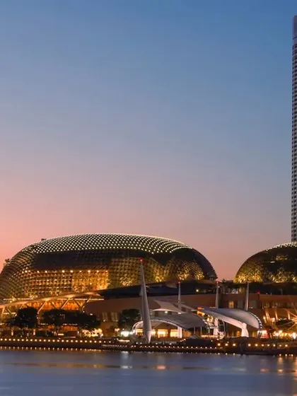 The iconic Esplanade Theatres on the Bay in Singapore, captured at sunset. The unique durian-shaped domes of the building glow against the twilight sky, showcasing a masterpiece of modern architecture.