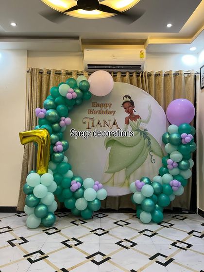 A charming Princess Tiana theme for a first birthday. The decoration features a custom backdrop of the Disney princess, framed by a beautiful balloon arrangement in shades of green and lilac.