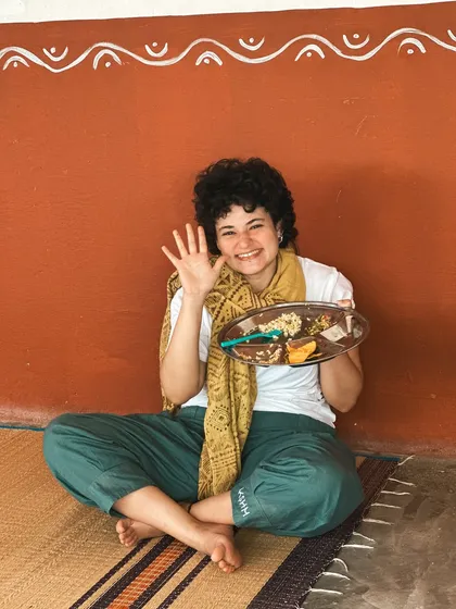 A student smiles as she holds her plate of sattvic food. Our meals are simple, delicious, and designed to support a clear mind and healthy body.