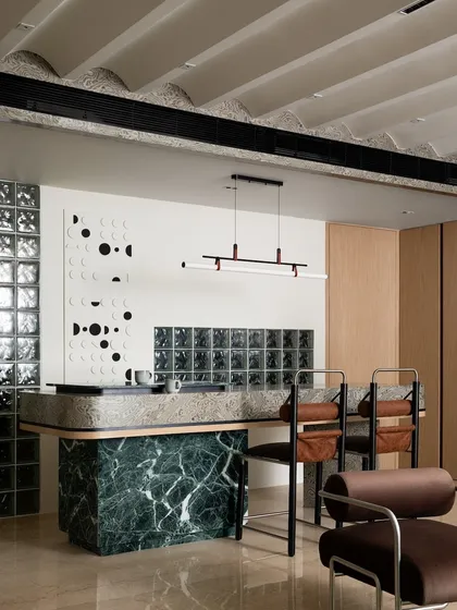 The breakfast counter is a masterpiece of mixed materials, with a green marble base, textured veneer top, and a backdrop of glass blocks and custom wall art.