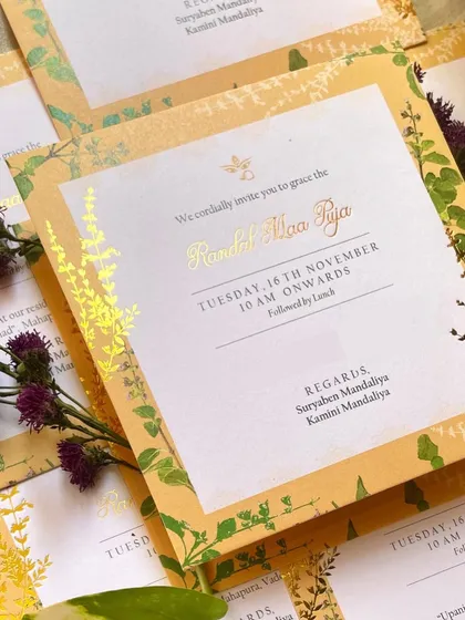 The 'Randal Maa Puja' invitation, featuring a warm yellow background with a delicate border of Tulsi illustrations and gold foil details.