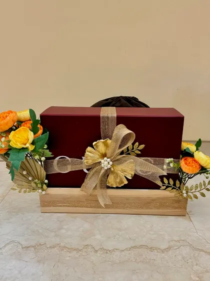 A single wedding gift elegantly wrapped and placed on a wooden platter, decorated with yellow-orange florals and golden accents.