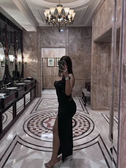 A mirror selfie in a luxurious marble bathroom, wearing a black high-slit gown for a fashion show.