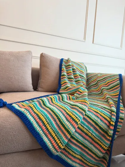 A vibrant, multi-colored striped throw with a bold blue border, adding a splash of color and texture to a neutral-colored couch.