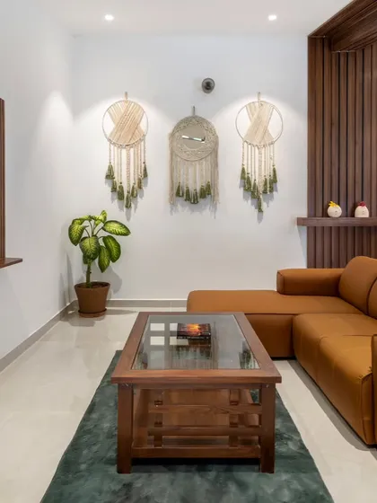 A comfortable living area with a tan sectional sofa and a dark wood coffee table. The macrame wall hangings and vertical wooden slats add texture and a touch of bohemian style to the room.