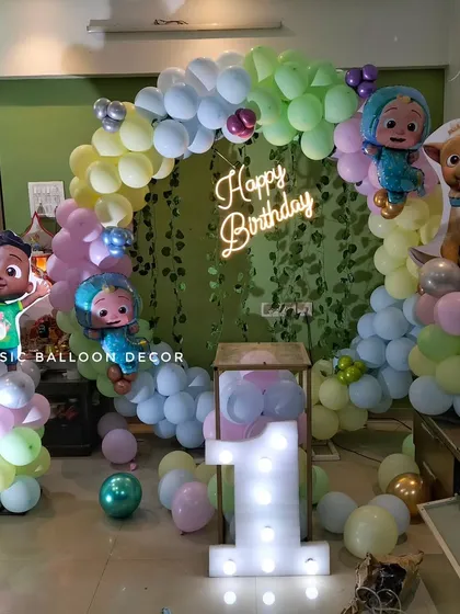 We brought the popular Cocomelon theme to life for this first birthday. The decoration includes a full balloon arch, a green wall backdrop, a 'Happy Birthday' neon sign, and cutouts of all the favorite characters.
