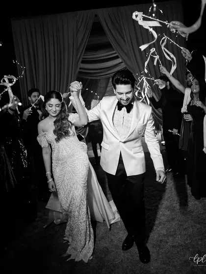The couple's grand entrance to their reception, celebrated by friends and family with ribbon wands under sparkling chandeliers.