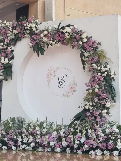 An elegant and classic engagement photo backdrop. We created this beautiful semi-circular arch with fresh lavender and white flowers, centered with the couple's custom wedding monogram.