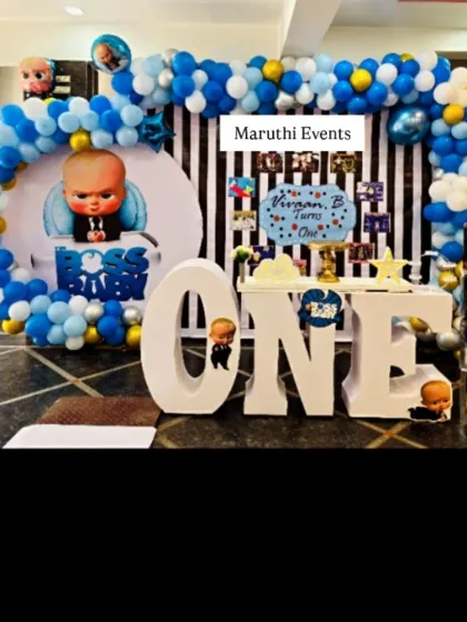 A "Boss Baby" first birthday party. The decor features a character backdrop, a blue and white balloon arch, and large light-up "ONE" letters.