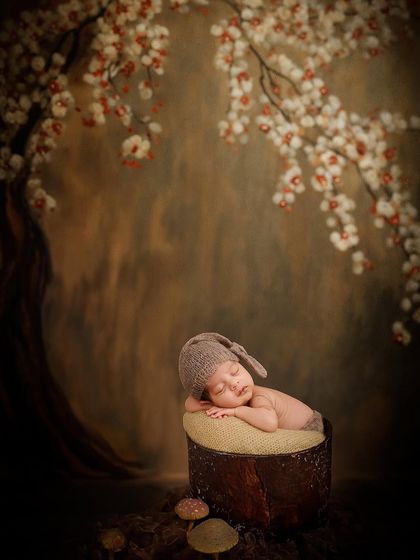 An artistic portrait of a newborn sleeping against a painted backdrop of a cherry blossom tree, blending rustic and fine-art styles.