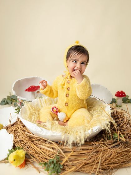 A cheeky little smile from this sweet baby chick. The soft yellow romper and matching bonnet complete this adorable, whimsical look.