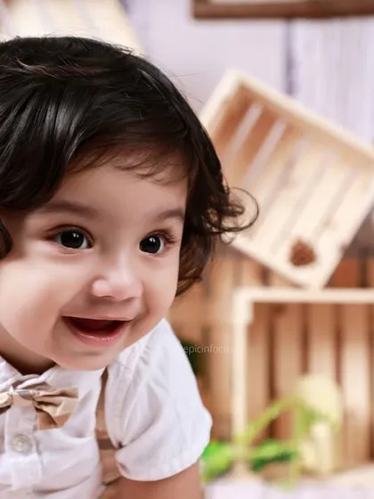A close-up shot capturing a moment of pure happiness. The wooden crates and bowtie add to the rustic charm of this classic toddler photoshoot.