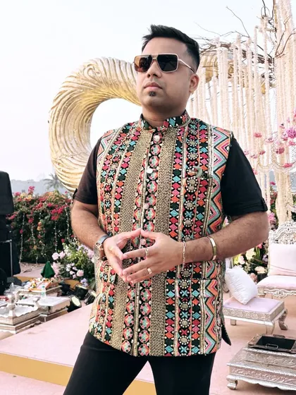 A profile shot showcasing the detailed embroidery of my semi-traditional jacket against the backdrop of an outdoor wedding setup.