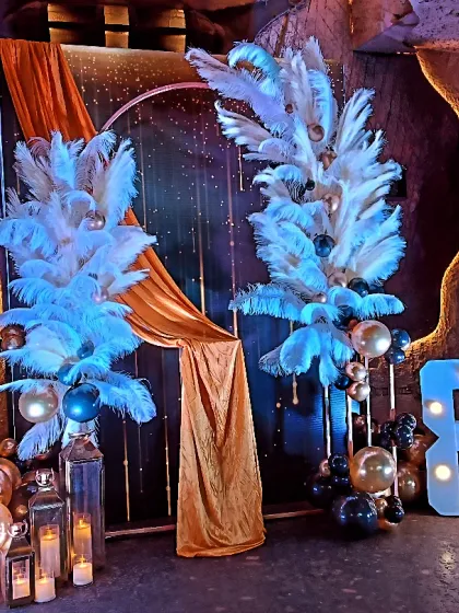 An absolutely stunning setup for an 80th birthday. I used a dramatic backdrop with large white feather plumes, gold draping, and marquee numbers to create a luxurious and celebratory atmosphere.