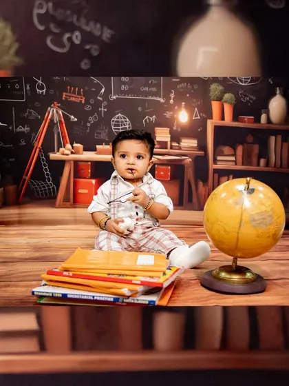 A creative 'little scholar' themed shoot, with the baby surrounded by books, a globe, and a chalkboard backdrop.