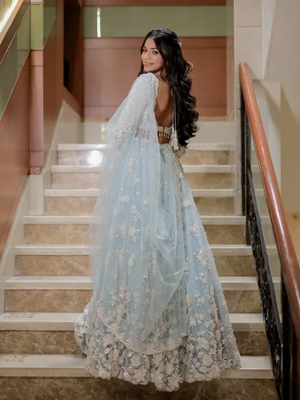 A classic bridal portrait from the back, looking over the shoulder. This pose beautifully displays the intricate back design of the blouse and the flowing drape of the dupatta.