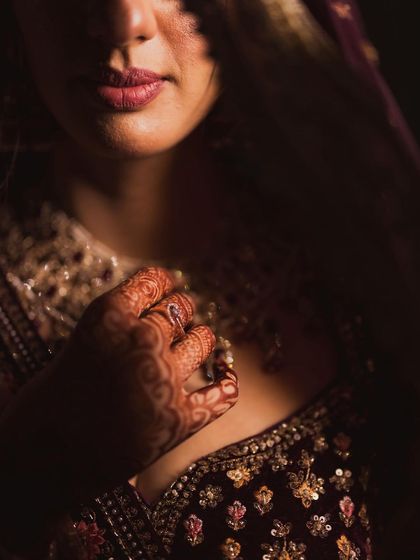 An artistic close-up focusing on the bride's lips and the intricate henna on her hand, capturing the sensual details of her look.