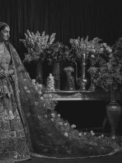 The bride in monochrome, her intricate lehenga and the floral decor taking on a timeless, ethereal quality. This artistic shot highlights the beauty of tradition in a classic format.
