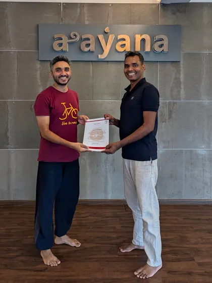 A smiling graduate accepts his certificate, ready to share the practice of yoga with the world.