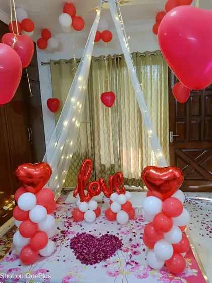 A classic red and white romantic room decoration. I created a beautiful canopy with fairy lights over the bed, flanked by balloon pillars and a "LOVE" message, with a heart made of rose petals as the centerpiece.